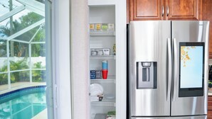 Une cuisine équipée d’un réfrigérateur en acier inoxydable et d’une porte en verre donnant sur l’espace piscine.