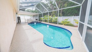 Une piscine intérieure offrant une vue dégagée sur la végétation environnante, ainsi qu’un espace abrité avec une table et des chaises.