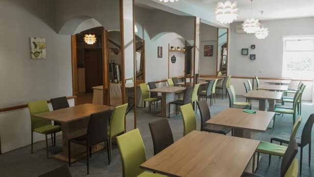 Een moderne eetruimte met houten tafels en groene stoelen, met een centrale trap en uitzicht op de omgeving.