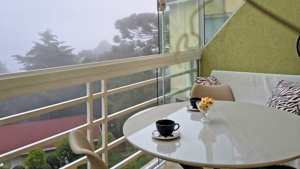 Ein Balkon mit Glastrennwand, ein runder Tisch mit Tasse und Untertasse sowie ein Sitzkissen mit Zeprazmuster.