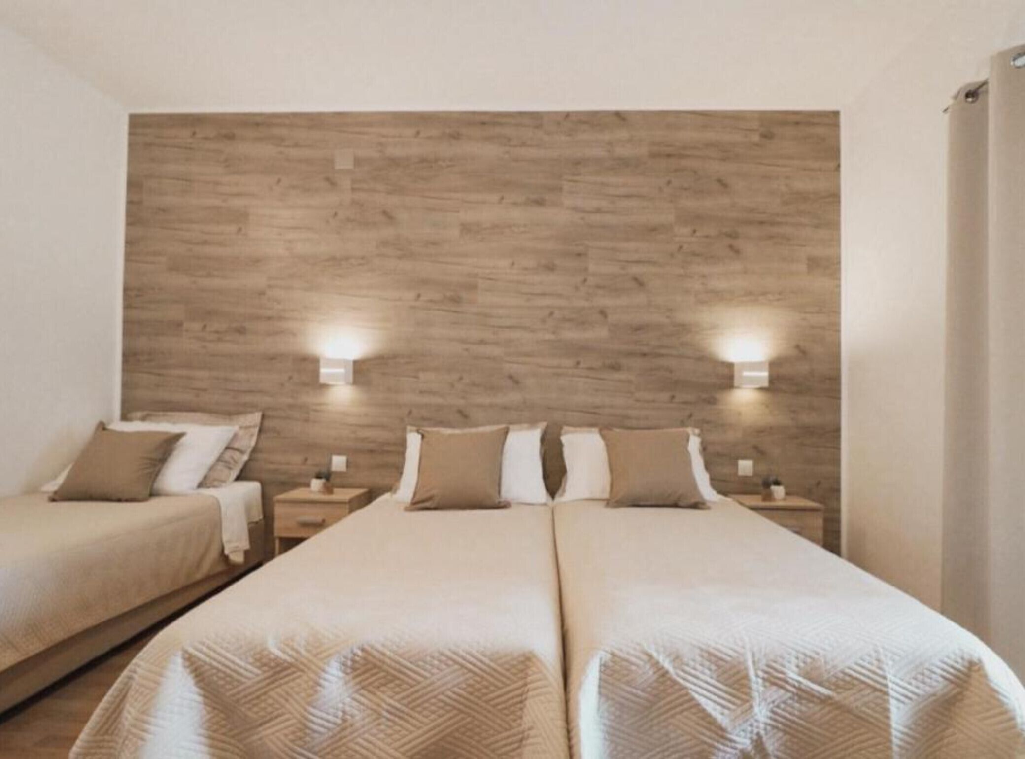 Une chambre d’hôtel avec deux lits, une tête de lit en bois, des lampes de chevet et une décoration aux couleurs neutres.