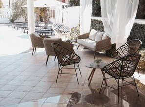 Un espace extérieur aménagé avec des chaises et un canapé en osier, une petite table ronde et un auvent blanc.