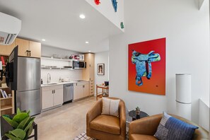 A modern kitchen with stainless steel appliances, a dining area with a brown leather sofa, and a vibrant painting on the wall. - Hotel SOMA (Fort Worth)