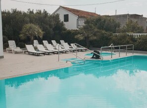 Piscina com espreguiçadeiras brancas e um trampolim.