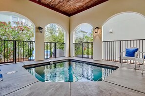 A swimming pool with a wooden ceiling and arched windows, surrounded by a white railing and a chair with a blue cushion. - Villa Palmeira (Santa Rosa Beach)