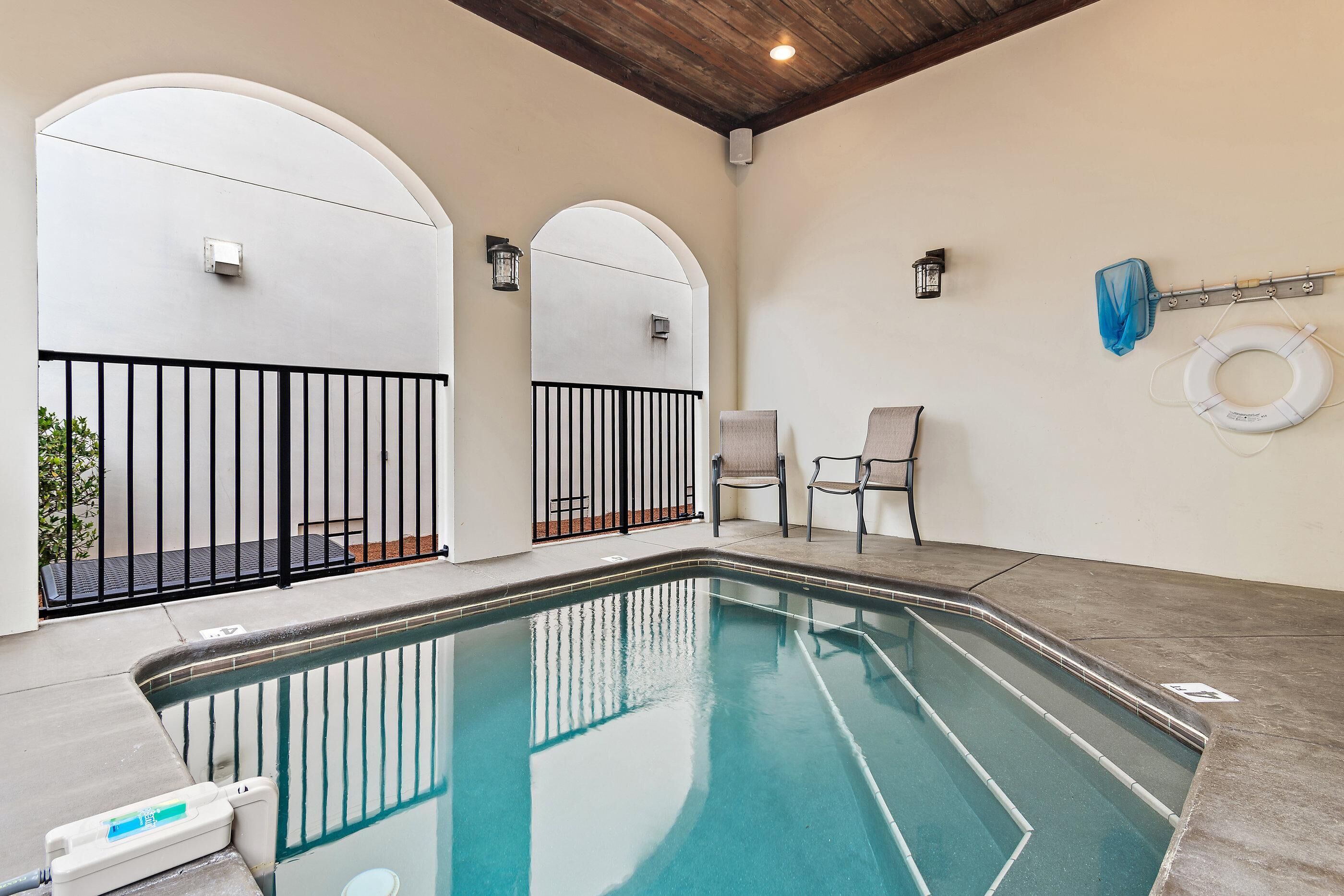 An indoor swimming pool with a concrete floor, black metal railings, and a lifebuoy on the wall.
