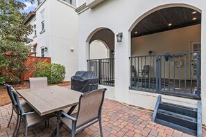 An outdoor patio with a table and chairs, a covered grill, and a view of the building's interior through an archway. - Villa Palmeira (Santa Rosa Beach)