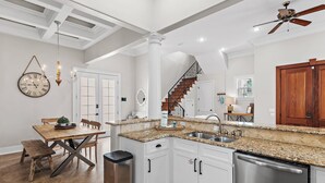 Une cuisine avec des meubles blancs, des plans de travail en granit, un lave-vaisselle en acier inoxydable et un escalier en bois.