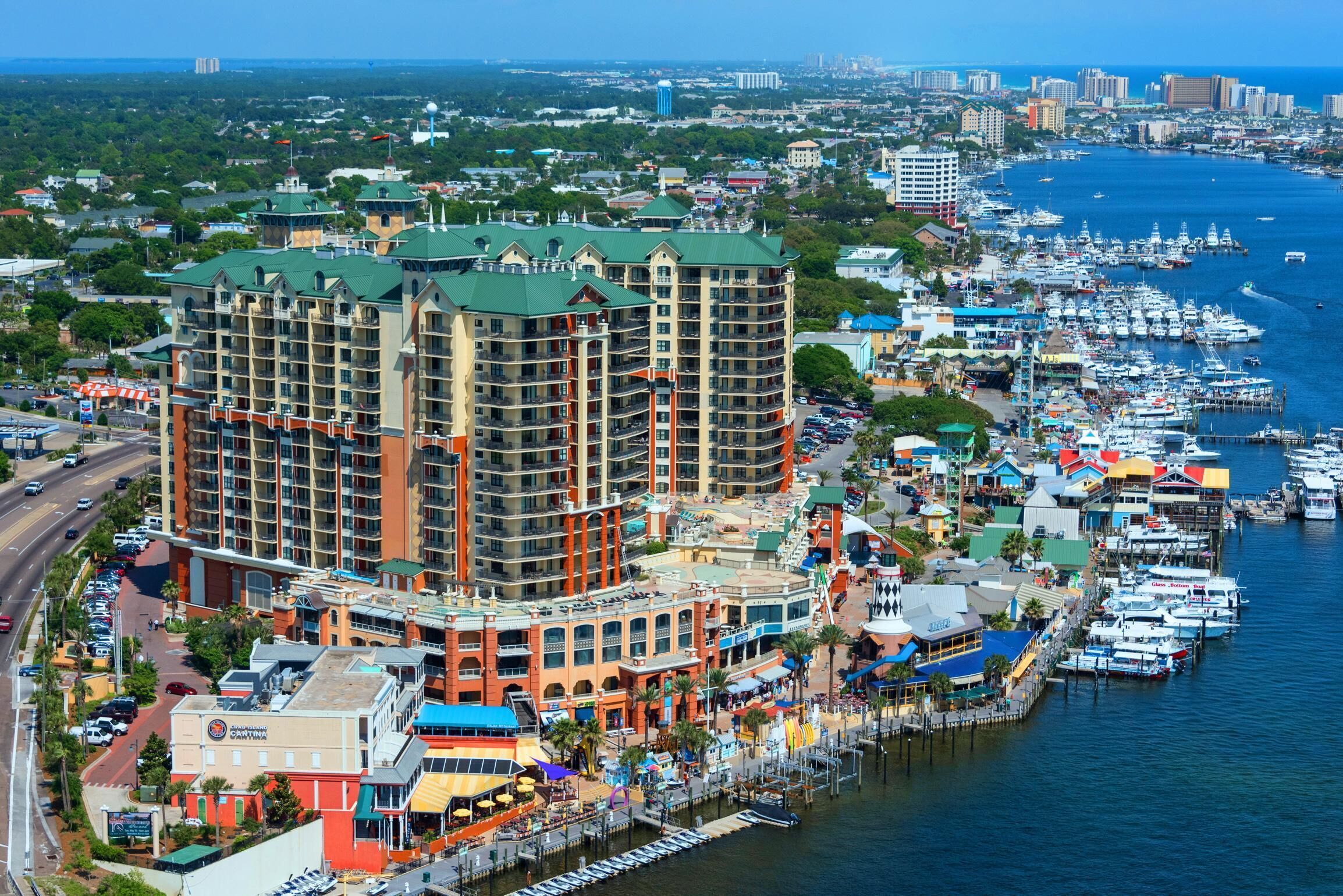 A high-rise hotel with multiple floors, a marina with boats, and a coastal cityscape in the background.