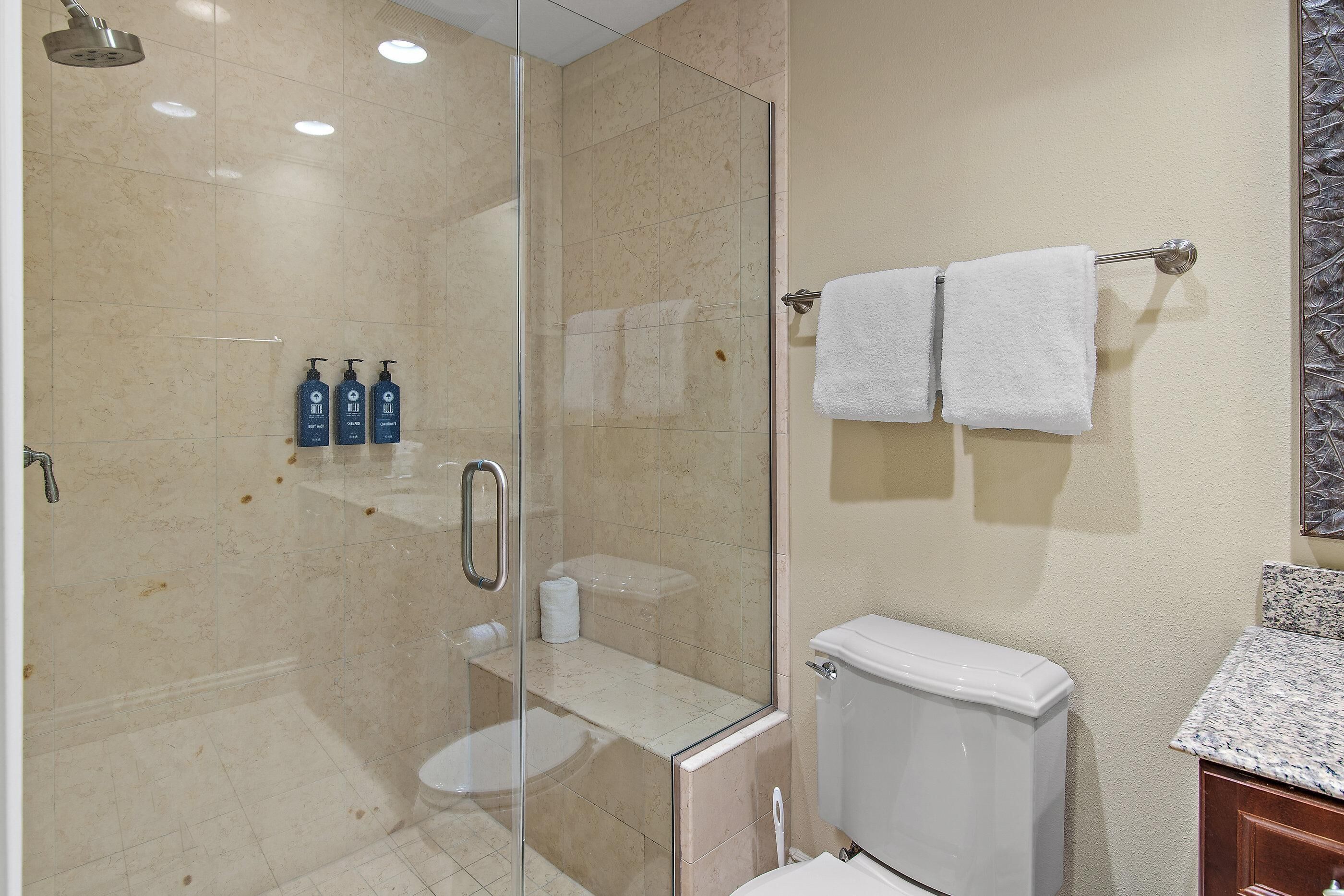 A bathroom with a glass-enclosed shower, a toilet, and a sink with a granite countertop.
