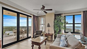 A spacious living room with a large window, a ceiling fan, a sofa, a coffee table, and a chair. - Emerald Grande E810 (Destin)