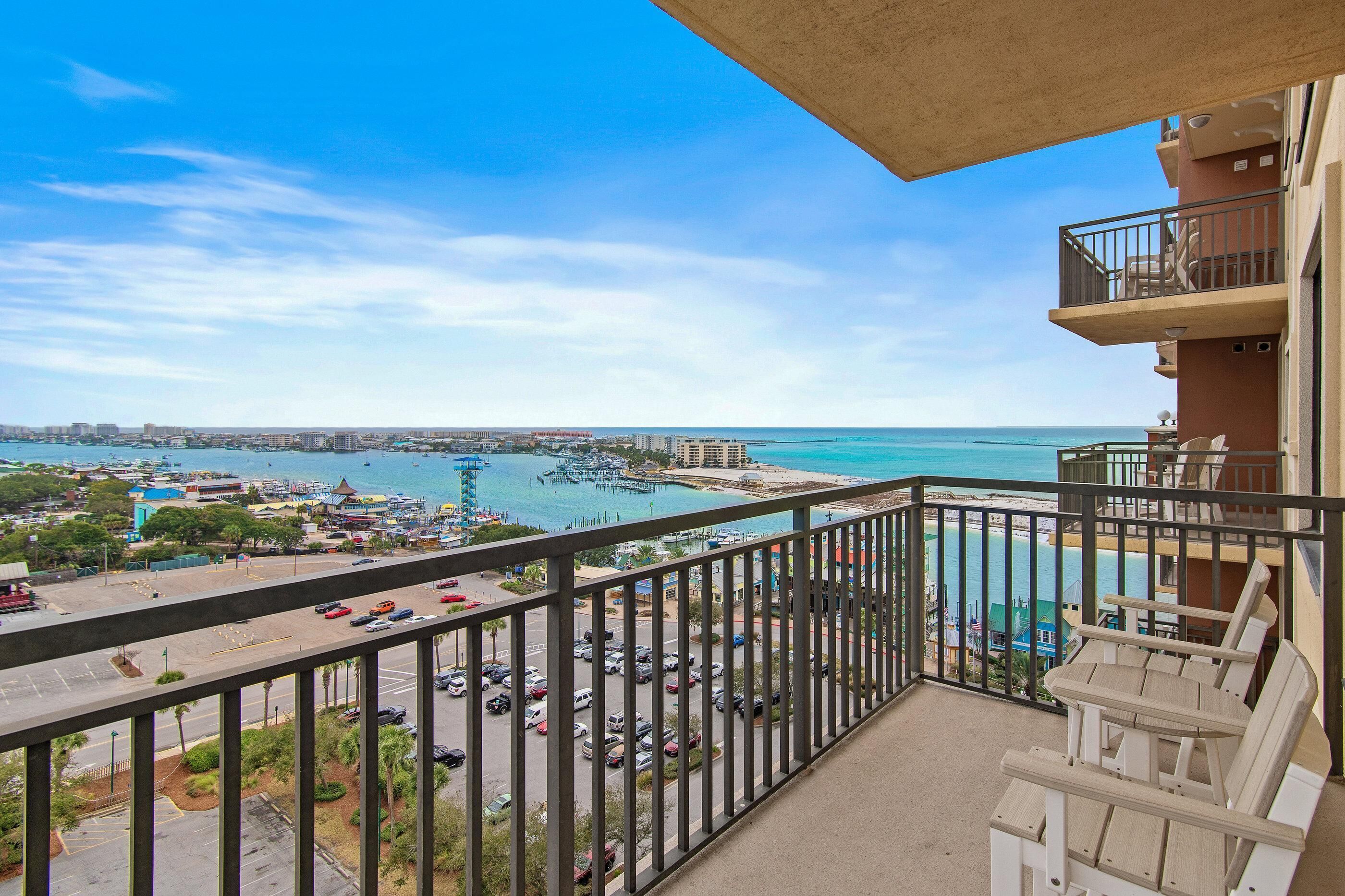 A balcony with a view of a marina, a parking lot, and a beach.
