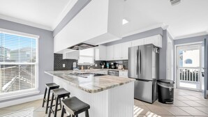 A modern kitchen with a central island, bar stools, stainless steel appliances, and a view to the outside. - Serenity at Sunnyside (Panama City Beach)