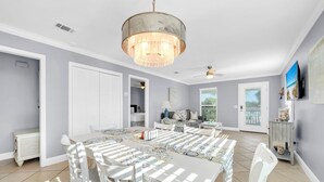 A spacious dining area with a large table and chairs, a chandelier, and a view of the outdoors. - Serenity at Sunnyside (Panama City Beach)