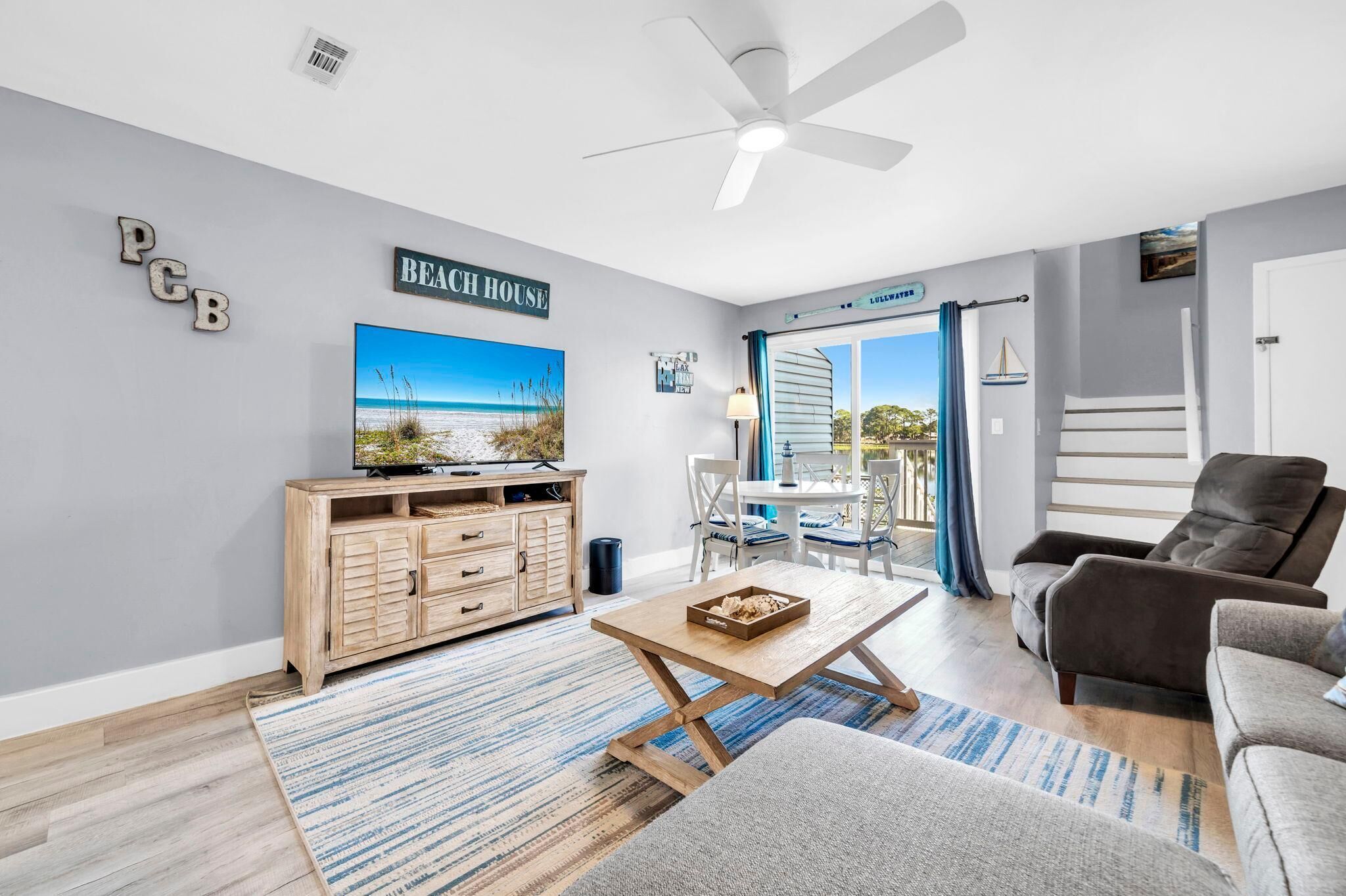 A beach-themed living room with a television, a wooden cabinet, a coffee table, and a grey sofa.