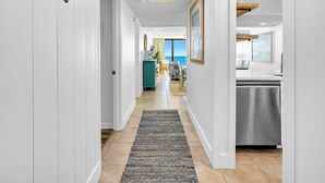 A hallway with white walls, a patterned rug, and wooden wall decor. - Edgewater Tower 3-1003 (Panama City Beach)