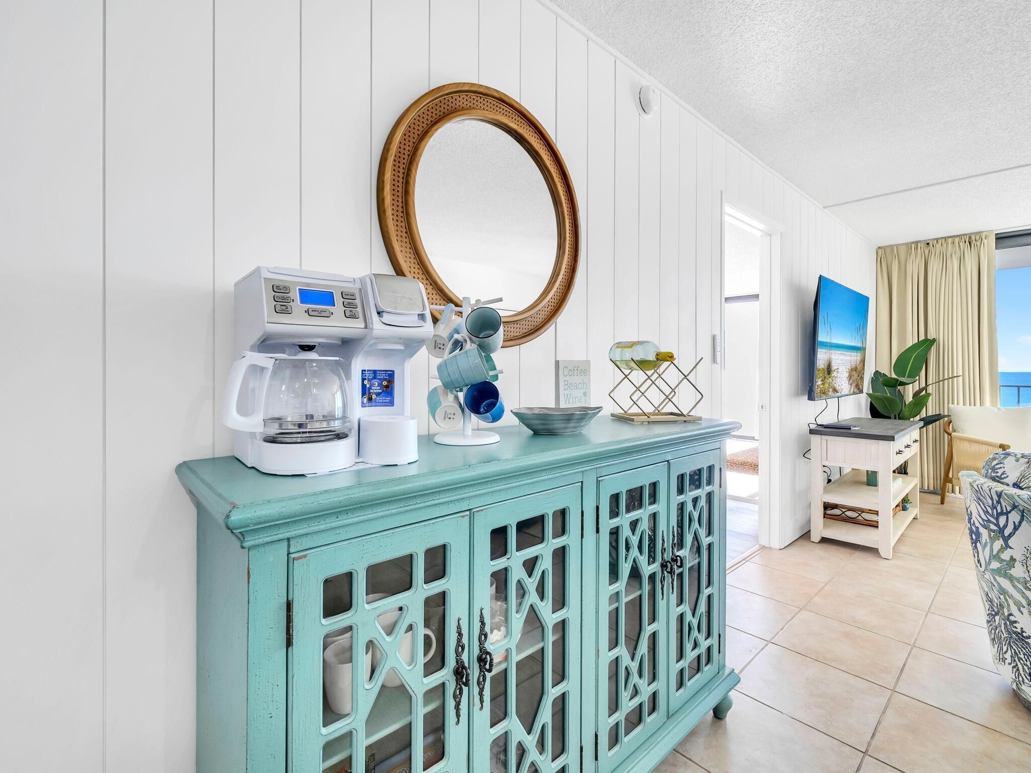 A room with a teal cabinet, a coffee maker, a mirror, and a television.