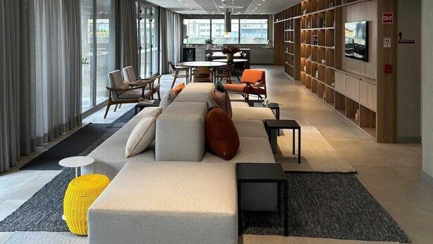A modern lounge area with a sofa, chairs, a small table, and a bookshelf. - Studios with outdoor pool in the lounge. (São Paulo)