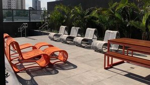 A rooftop terrace with outdoor seating, including orange and white chairs, and a wooden table. - Studios with outdoor pool in the lounge. (São Paulo)