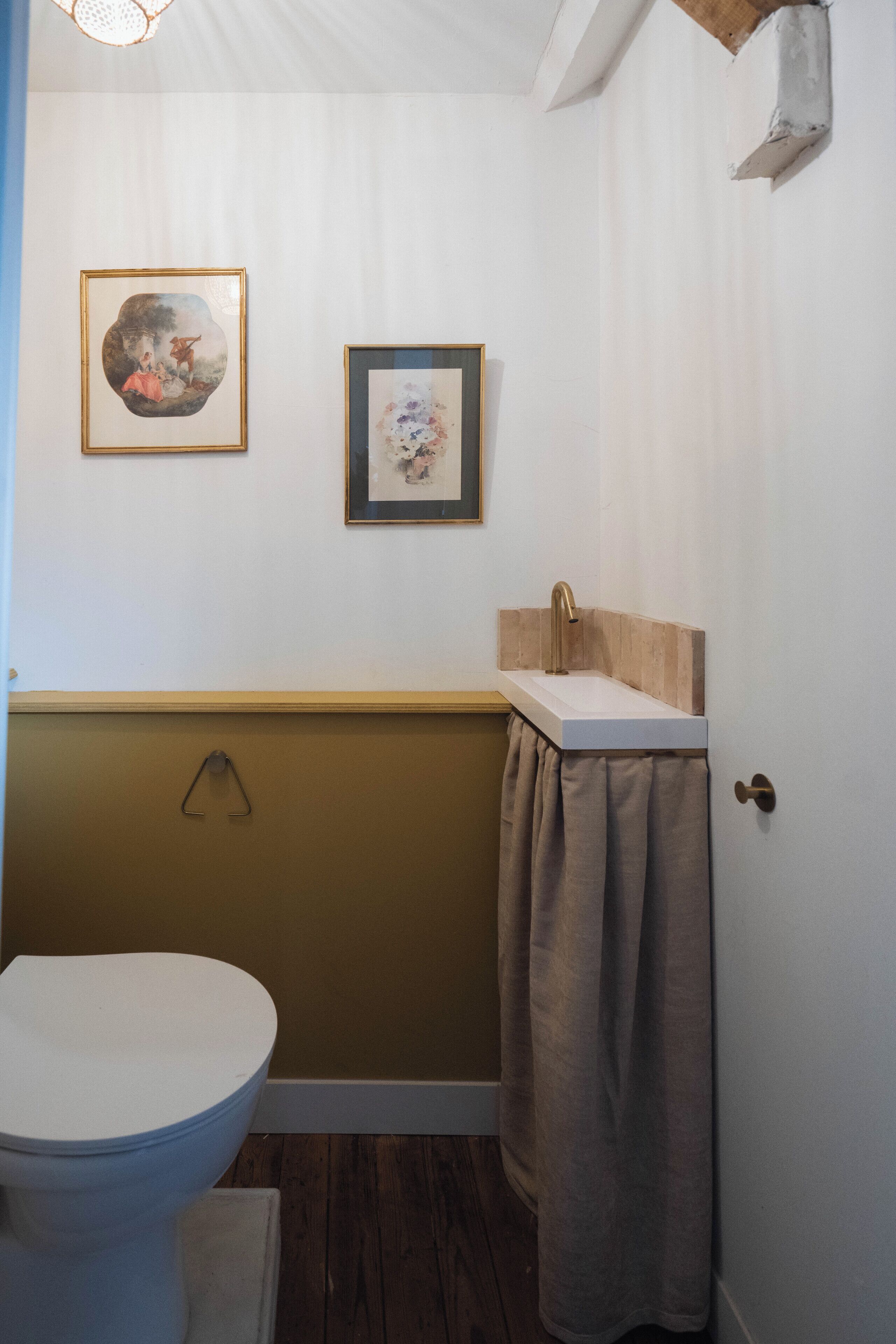 Et badeværelse med toilet, vask og to billeder hængende på væggen.