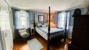 Una cama con dosel en una habitación con suelo de madera, una silla pequeña y una alfombra.