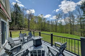 Een terras met Adirondack-stoelen, een vuurkuil en uitzicht op een gazon en bomen.