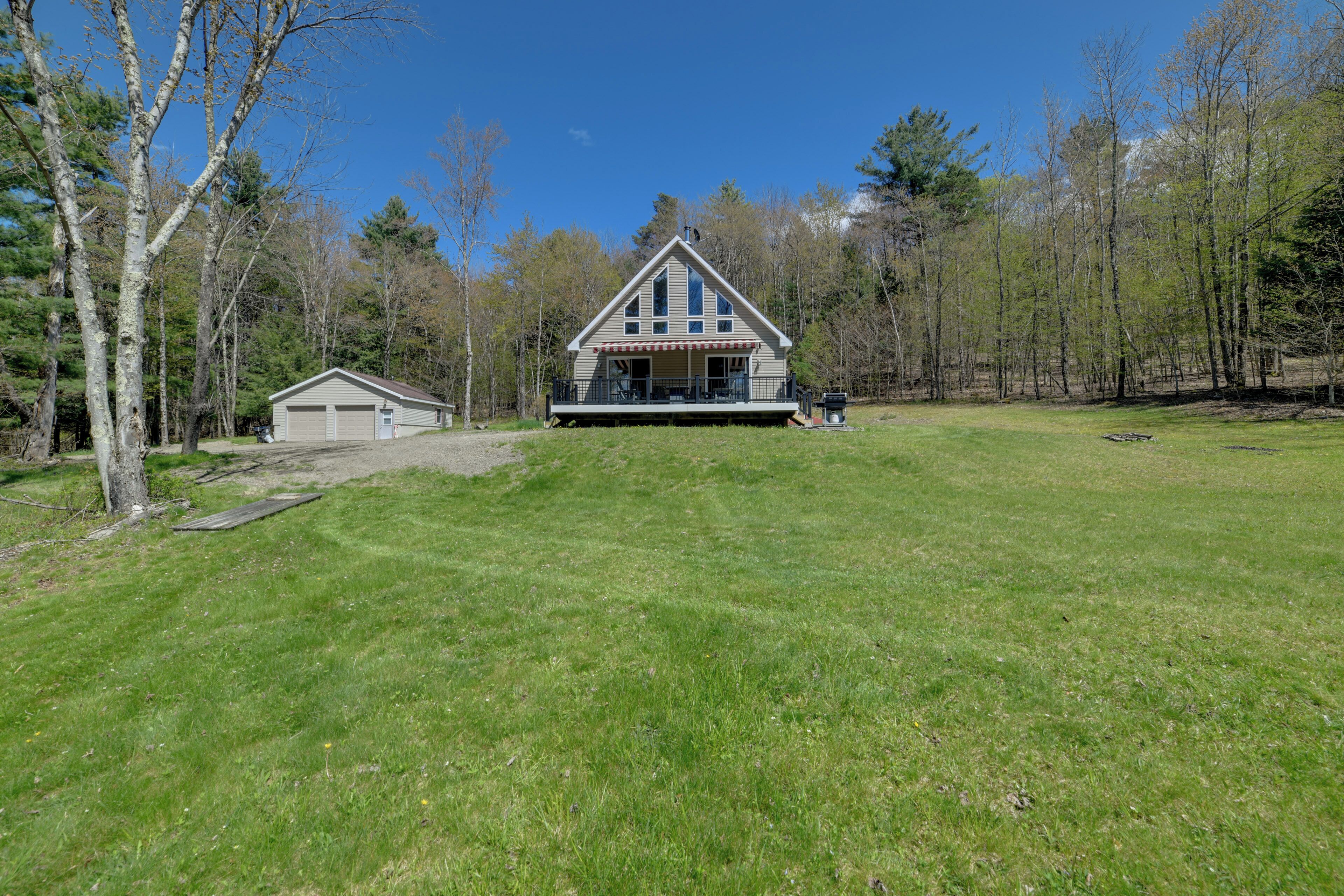 A two-story house with a large front porch, a garage, and a grassy yard surrounded by trees.