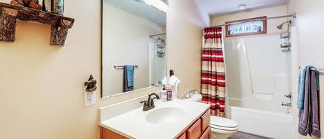 A bathroom with a large mirror, a sink, a toilet, and a shower.