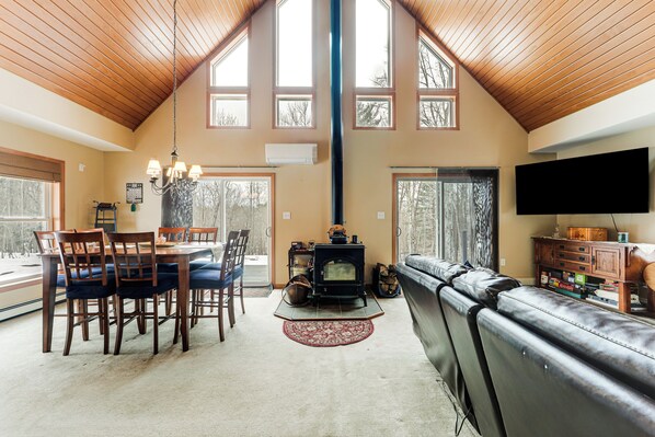 A spacious living area with a high ceiling, a fireplace, a dining table with chairs, and a leather sofa. - Mount Vision Home for Cooperstown Baseball Fams (Mt Vision)