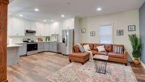 A modern kitchen with white cabinets, stainless steel appliances, and a brown leather sofa in a living area with a patterned rug. - Walk to Lititz Springs Park: Cozy Getaway! Apt 2 (Lititz)
