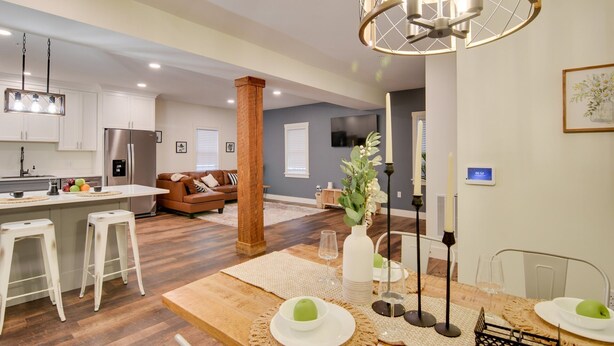 A modern kitchen with white cabinets, a stainless steel refrigerator, and a dining area with a wooden table and white stools. - Walk to Lititz Springs Park: Cozy Getaway! Apt 2 (Lititz)