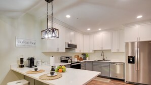 A modern kitchen with white cabinets, stainless steel appliances, and a central island with stools. - Walk to Lititz Springs Park: Cozy Getaway! Apt 2 (Lititz)