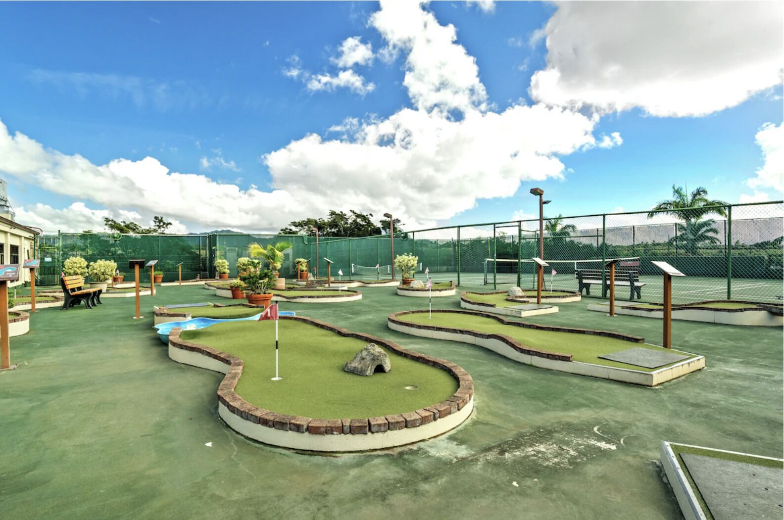 A miniature golf course with multiple holes, benches, and potted plants.