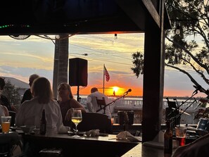 Un bar con vistas al atardecer, una bandera y un escenario con equipo musical.