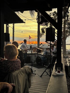 Un escenario al aire libre con equipo musical, una bandera estadounidense y vistas al atardecer.