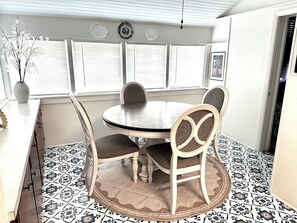 A dining area with a round table, four chairs, a vase with flowers, and patterned floor tiles.