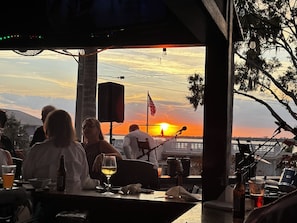 A bar with a view of the sunset, a flag, and a stage with musical equipment.