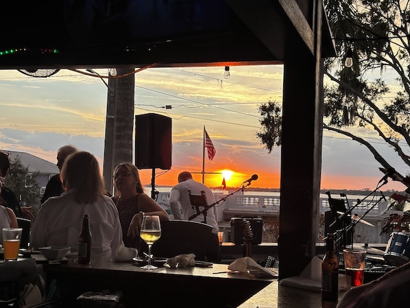 A bar with a view of the sunset, a flag, and a stage with musical equipment.
