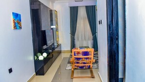 A hallway with a TV, a patterned chair, and a painting on the wall. - The Precision (Lagos)