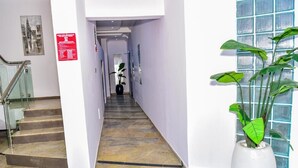 A hotel hallway with marble flooring, a staircase, a potted plant, and a blue glass partition. - The Precision (Lagos)