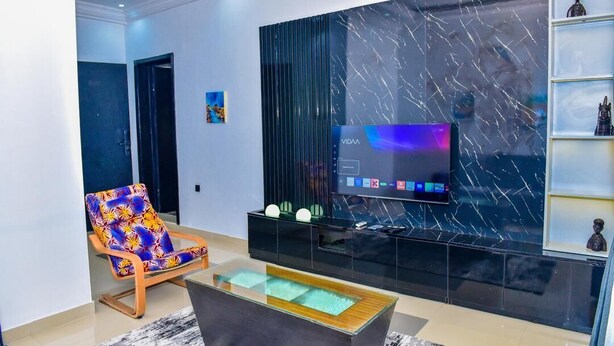 A modern living room with a flat-screen TV, a colorful chair, a glass coffee table, and a marble wall. - The Precision (Lagos)