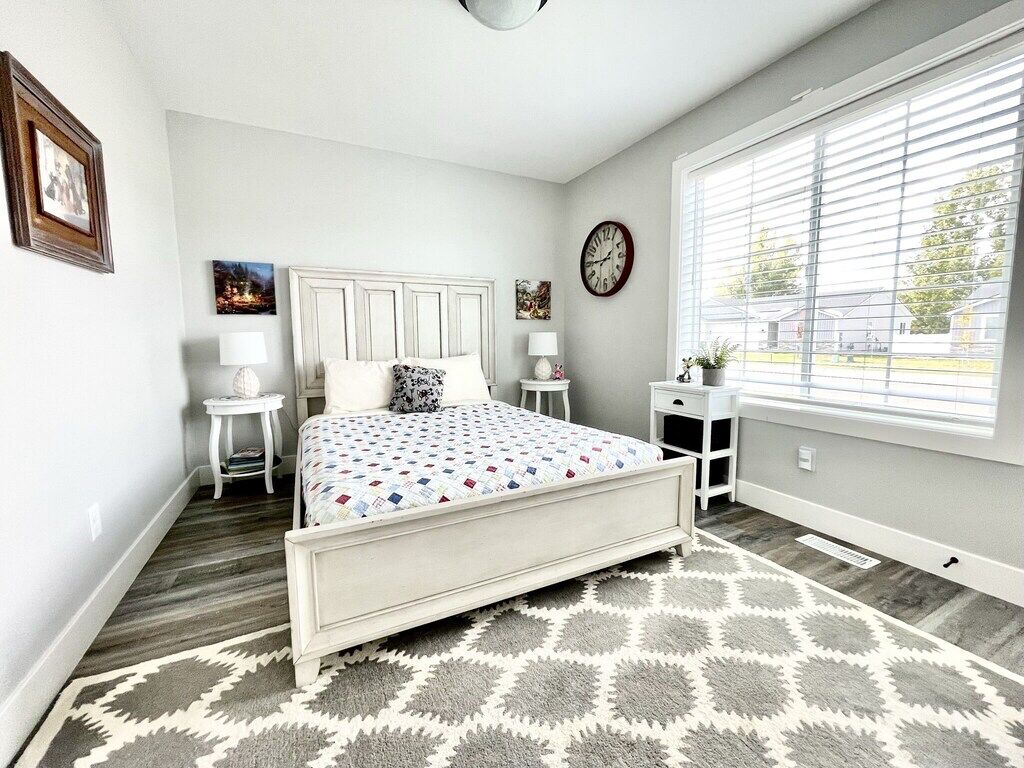 A bedroom with a bed, bedside tables, a clock, and a window with blinds.