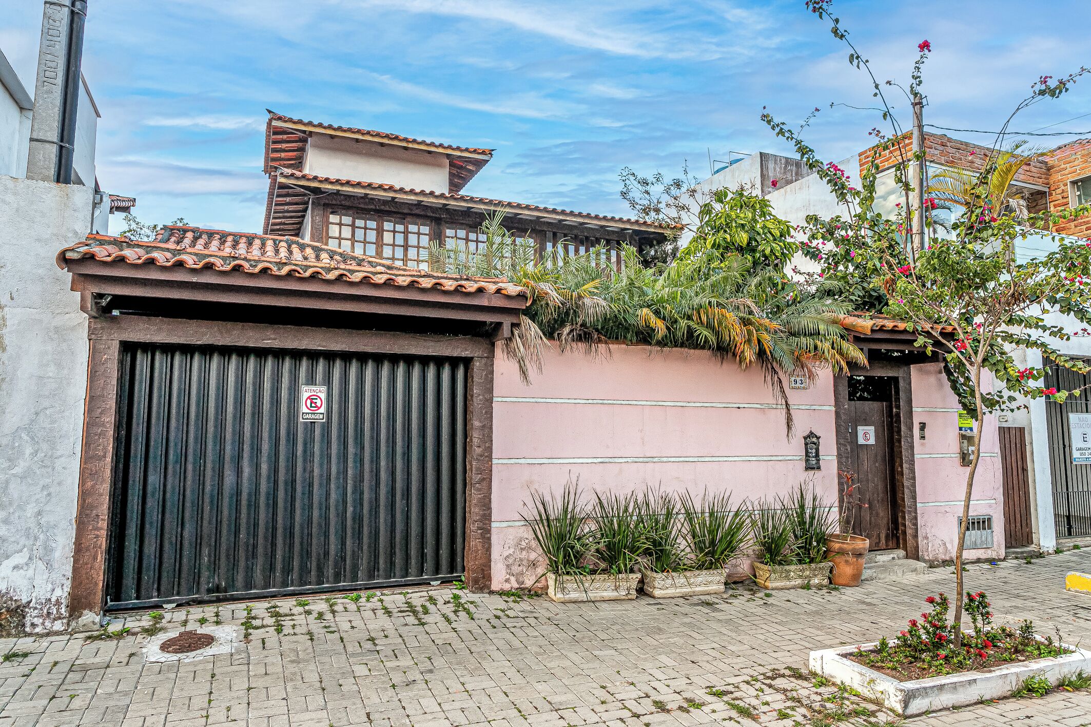 A building with a closed garage door, a pink wall, and a tiled roof.