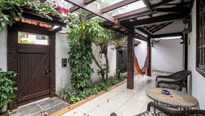 A covered patio with a wooden door, a table with chairs, and a hammock. - Cozy house with pool in the center of Buzios. (Buzios)
