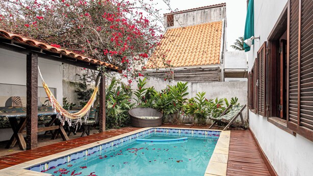 A swimming pool with a tiled edge, surrounded by a wooden deck and a covered seating area with a hammock. - Cozy house with pool in the center of Buzios. (Buzios)