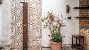 A tiled shower area with a wooden door, a potted plant, and a small table. - Cozy house with pool in the center of Buzios. (Buzios)