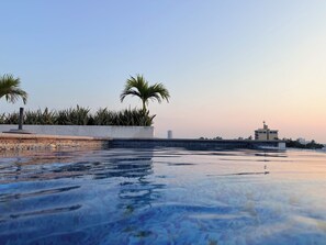 Ein Poolbereich mit zwei Palmen, einer gefliesten Terrasse und Blick auf entfernte Gebäude.