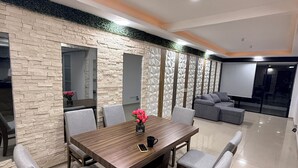 A modern dining area with a wooden table and grey upholstered chairs, a decorative vase with flowers, and a stone-textured wall.