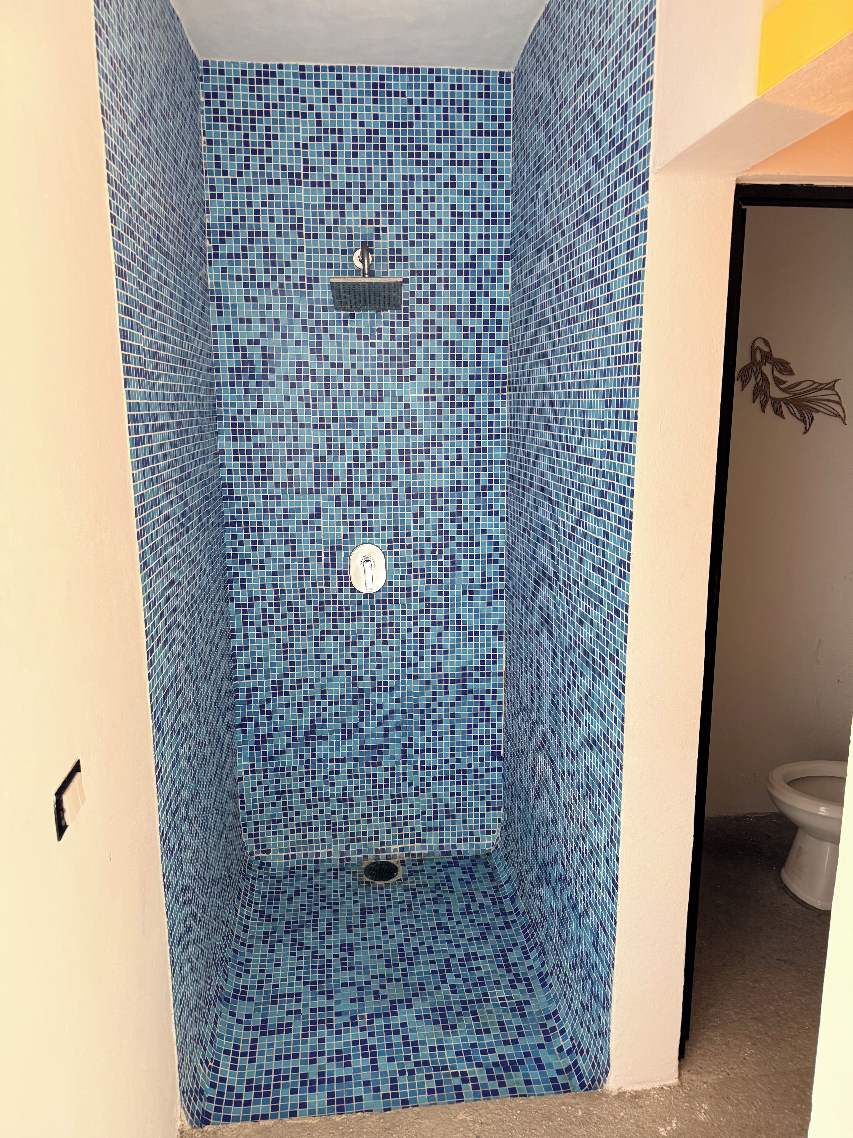 A bathroom with blue mosaic tile walls, a white toilet, and a shower area.