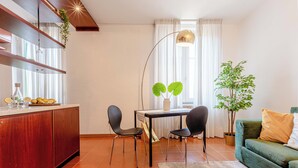 Uma sala de estar moderna com área de jantar, apresentando um aparador de madeira, duas cadeiras pretas, uma mesa de jantar, um sofá verde e um vaso com planta.